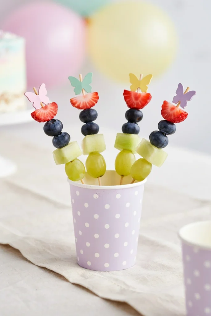 Fruit skewers dusted with glitter sugar standing upright in a glass for a fairy party dessert table