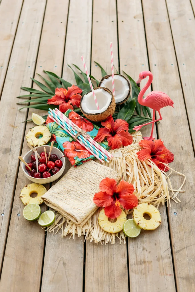 A full tropical party spread showing grass skirt, palm leaves, hibiscus flowers, straws, and flamingo accents together.