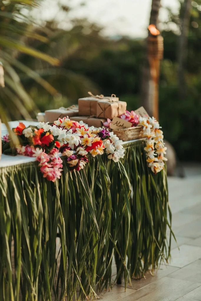 A gift table skirted in grass fringe with a stack of colorful leis draped over the edge
