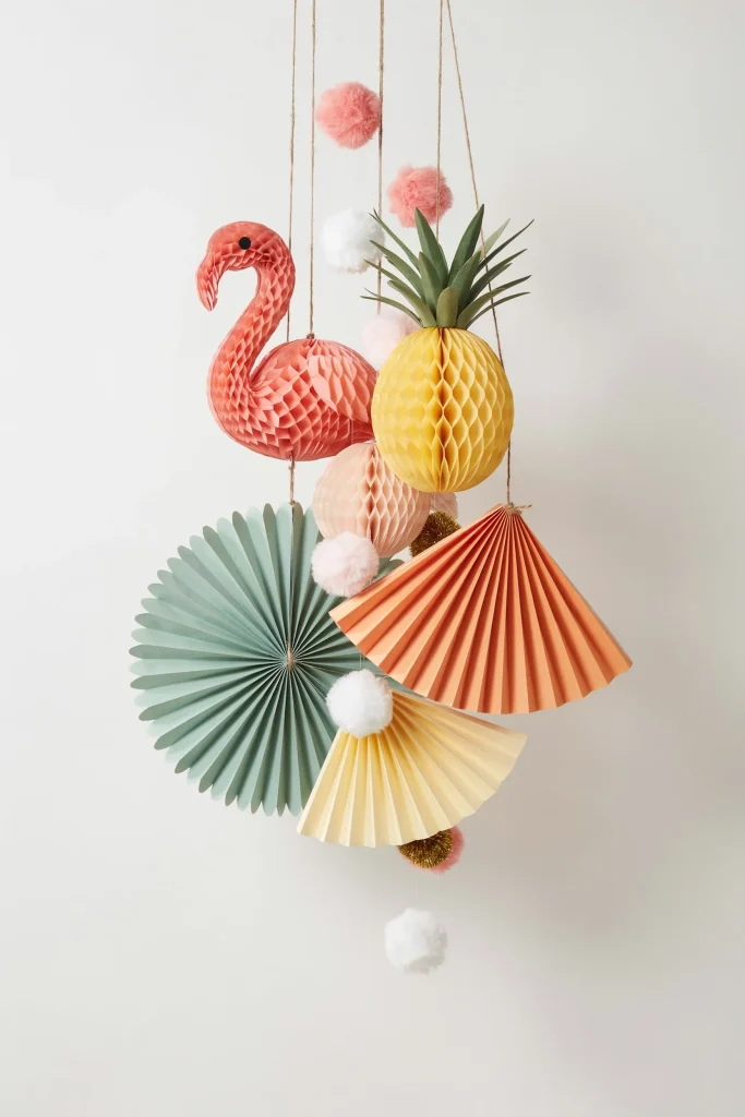 A cluster of honeycomb flamingo and pineapple decorations, paper fans, and pom-poms grouped together