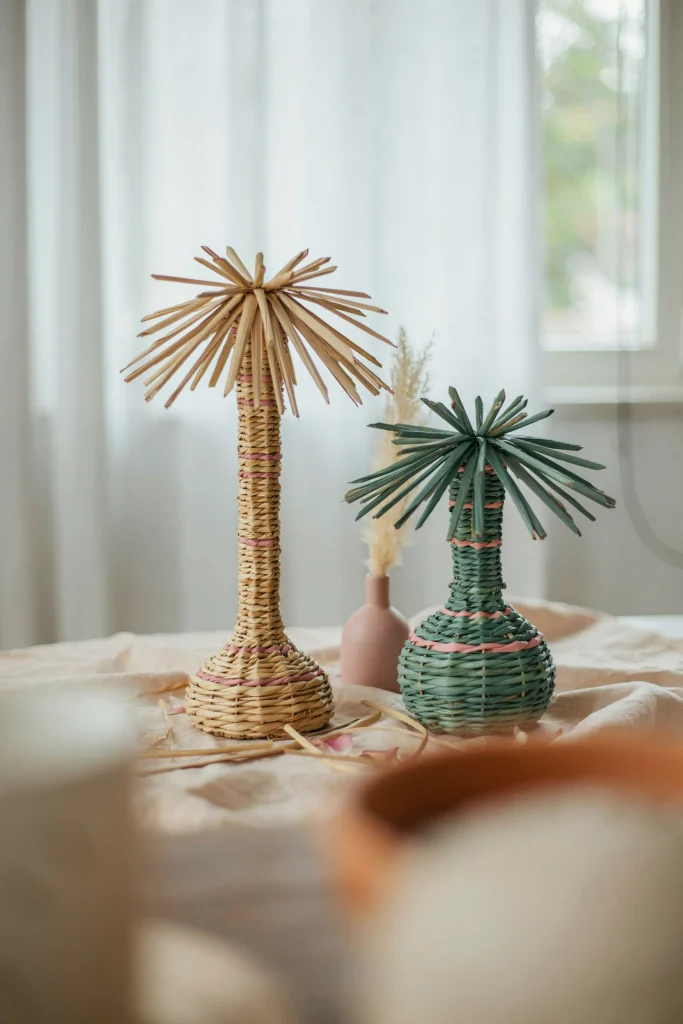 Two woven rattan palm tree centerpieces of different heights on a table, pink and green tones.