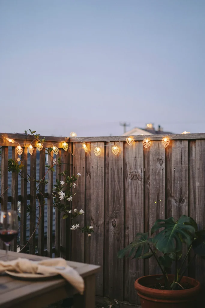 Monstera-shaped string lights glowing along a fence or patio edge at dusk.