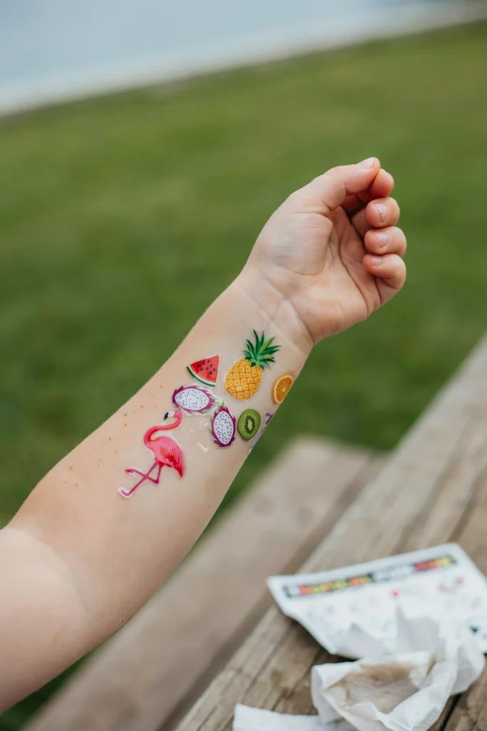 A child's arm decorated with colorful tropical fruit and flamingo temporary tattoos.