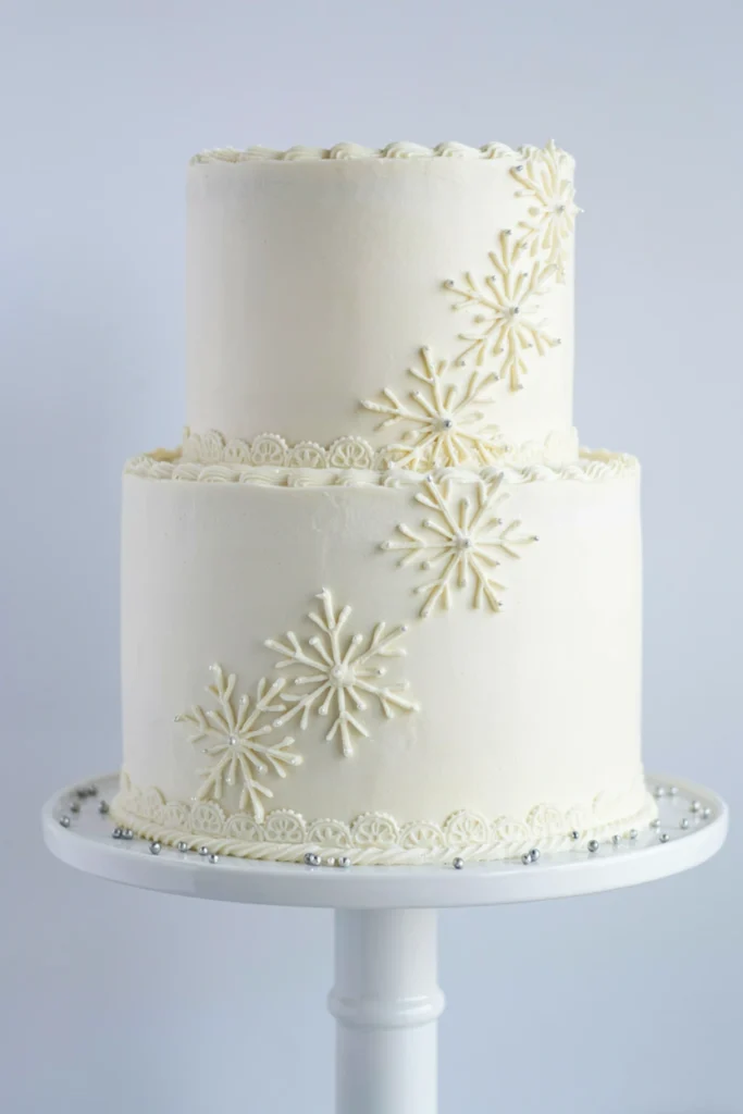 Two-tier white cake with three detailed piped buttercream snowflakes cascading down one side