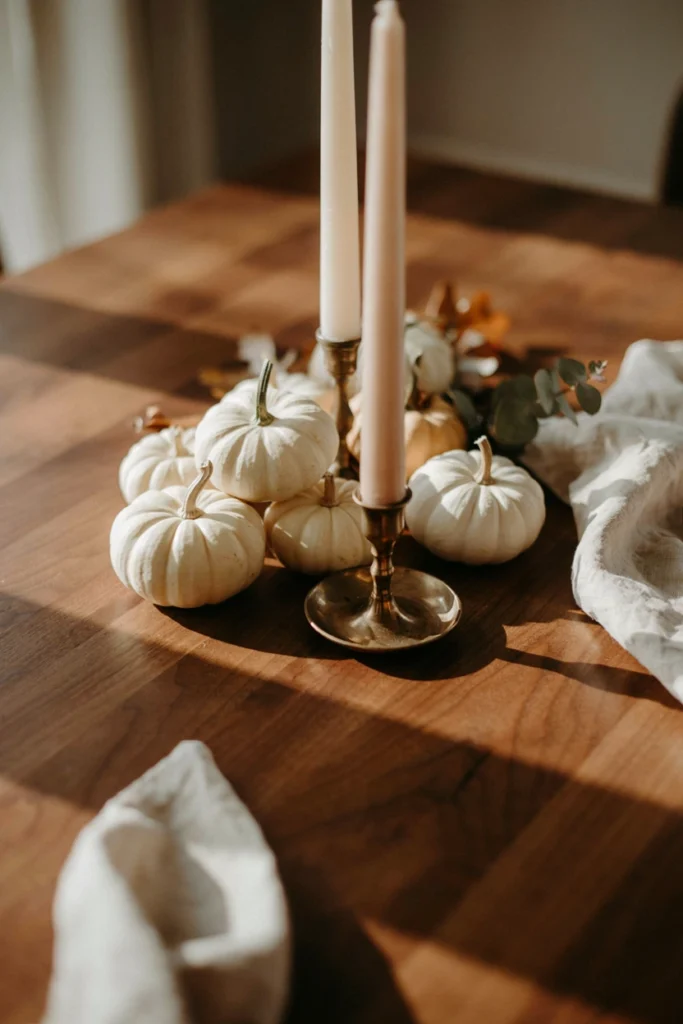 Mini white and cream pumpkins clustered around taper candles for a fall baby shower centerpiece