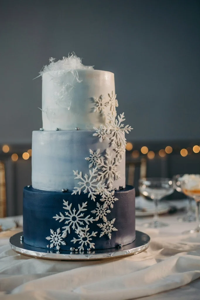 Tall three-tier cake deepening from white to navy with cascading fondant snowflakes and spun sugar detail