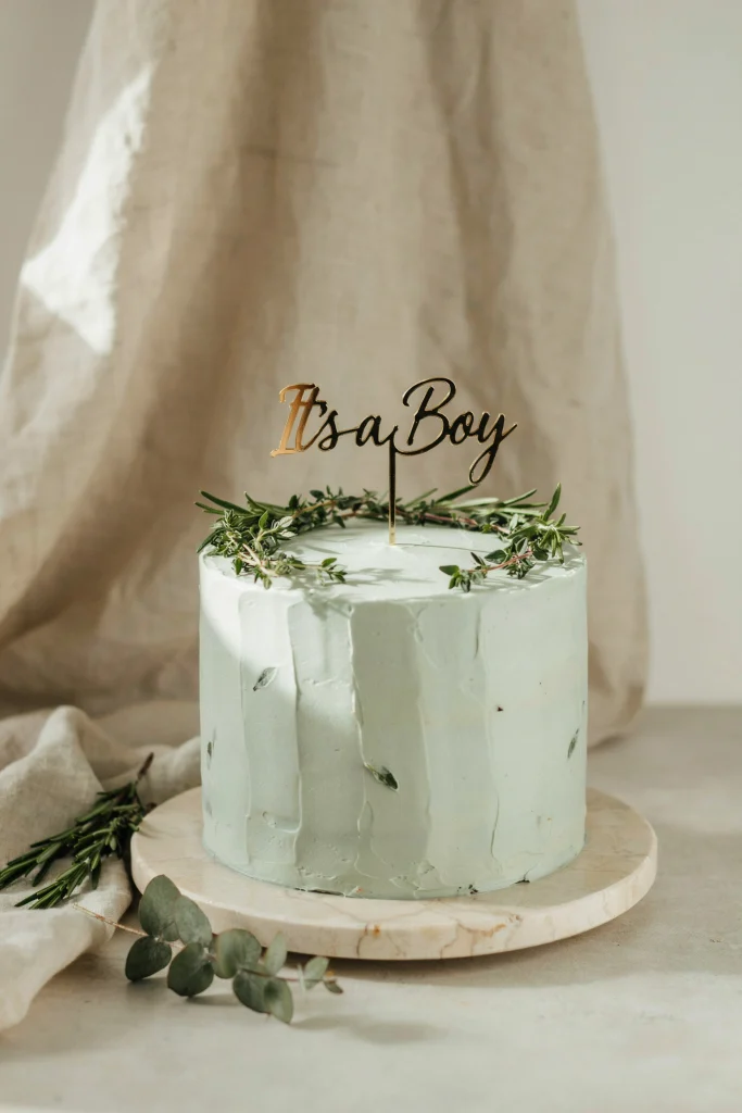 Sage green buttercream baby shower cake decorated with pressed herb leaves