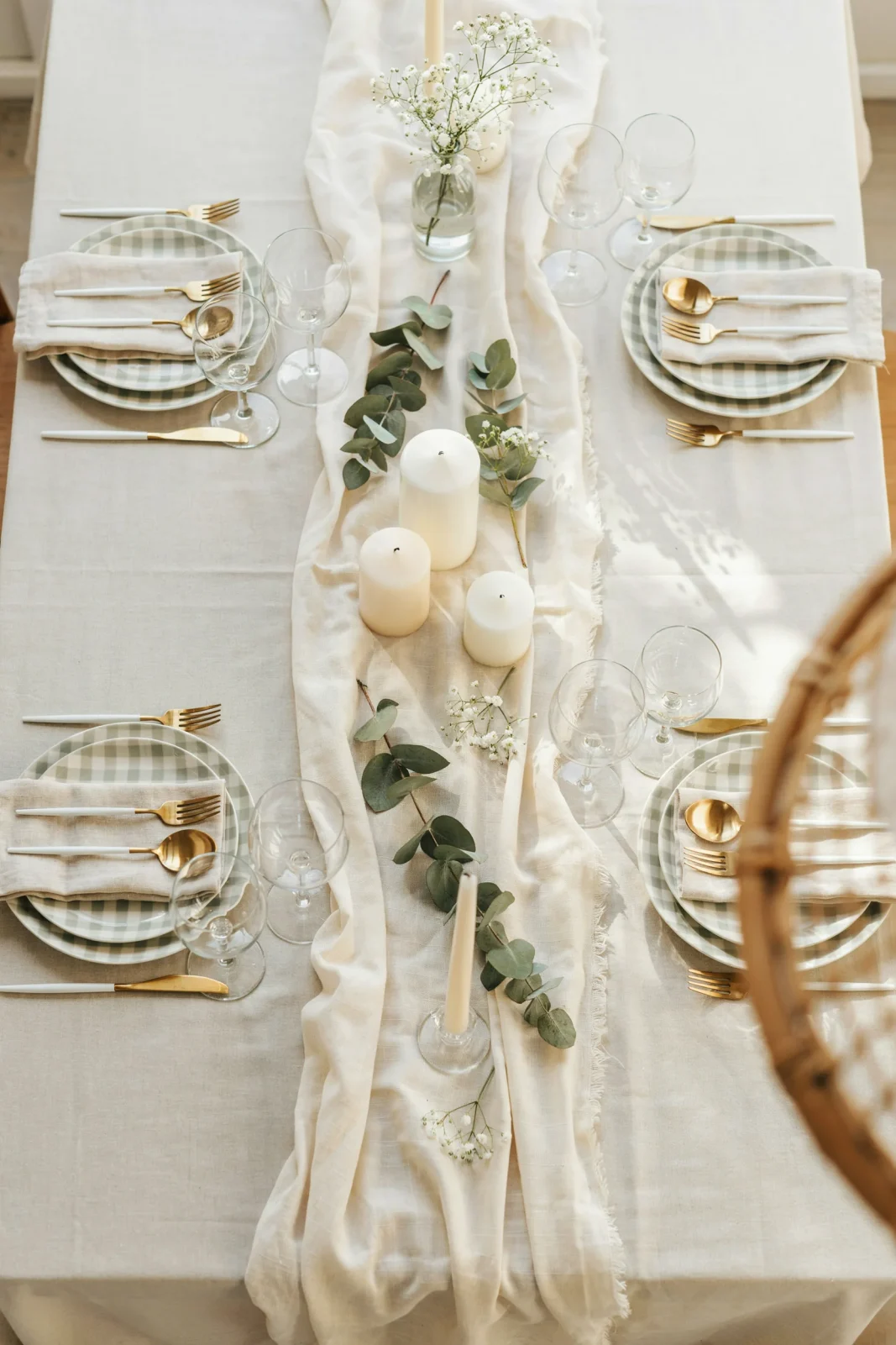 An overhead shot of a soft sage green baby shower tablescape with a cheesecloth runner, dried eucalyptus, and a small stack of gingham plates, warm natural light, no text overlay needed