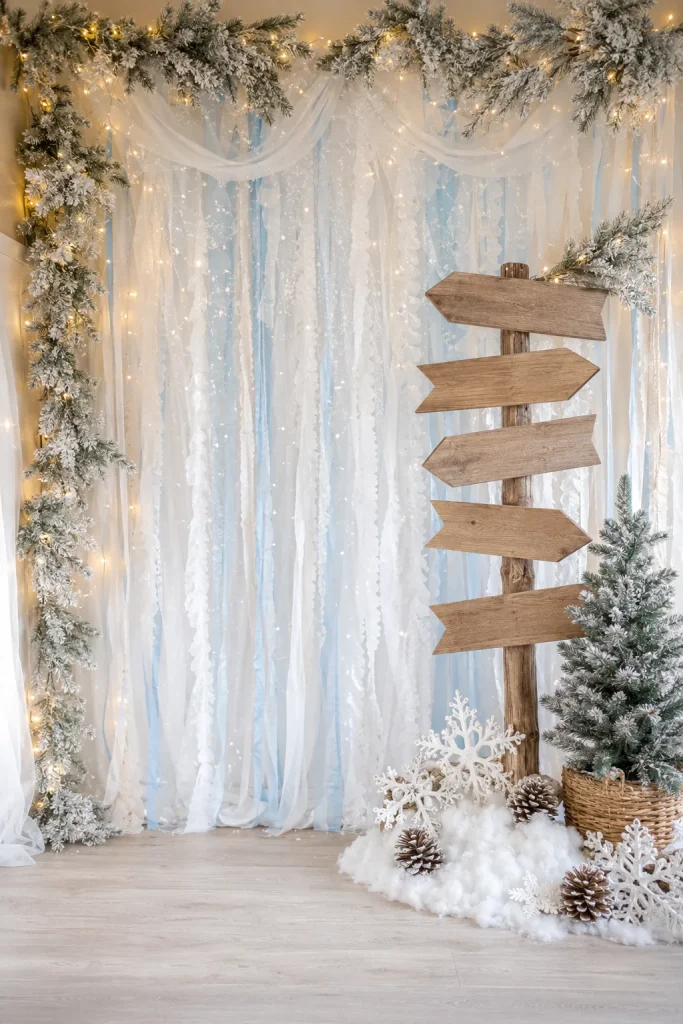 DIY North Pole photo backdrop with faux snow, icy blue streamers, and a wooden signpost prop
