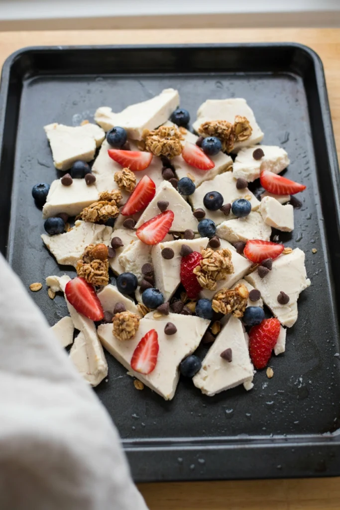 Pink yogurt bark studded with berries and granola, broken into pieces