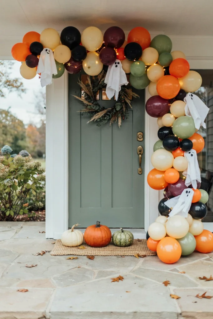 Orange, black and cream balloon garland ghost arch framing a doorway at a kids Halloween party